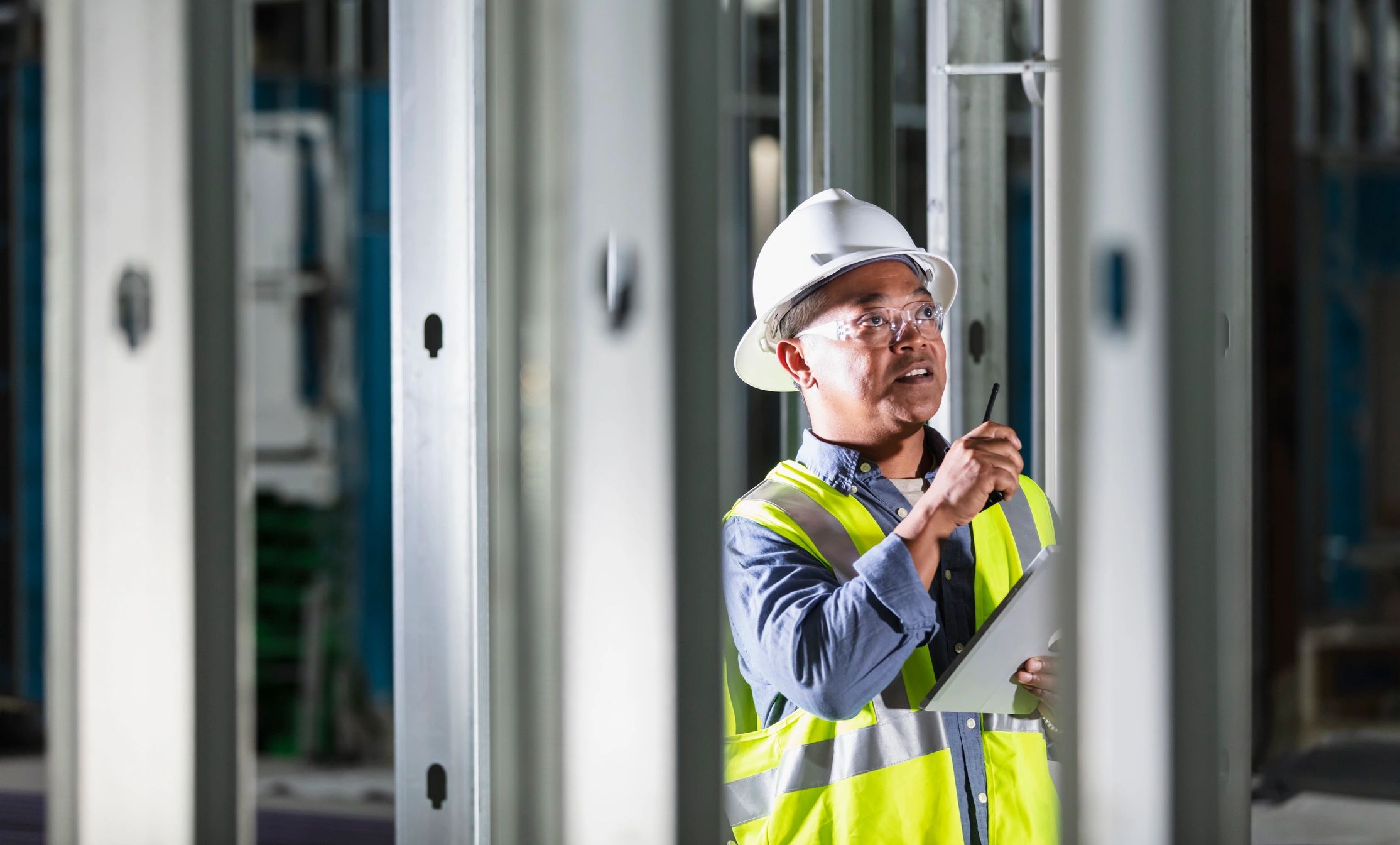 Engineer in hard hat using walkie-talkie and tablet at construction site